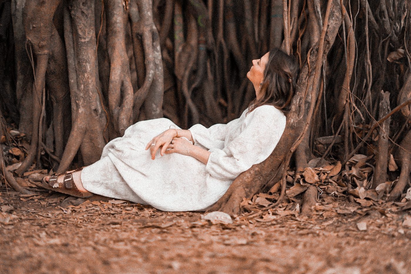 Femme apaisée adossée à un arbre, visage levé vers la lumière